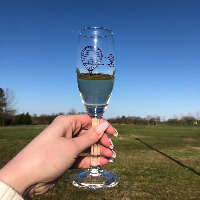 Claire's hand holding a champagne glass with hot air balloons given to the pair after getting engaged in the hot air balloon